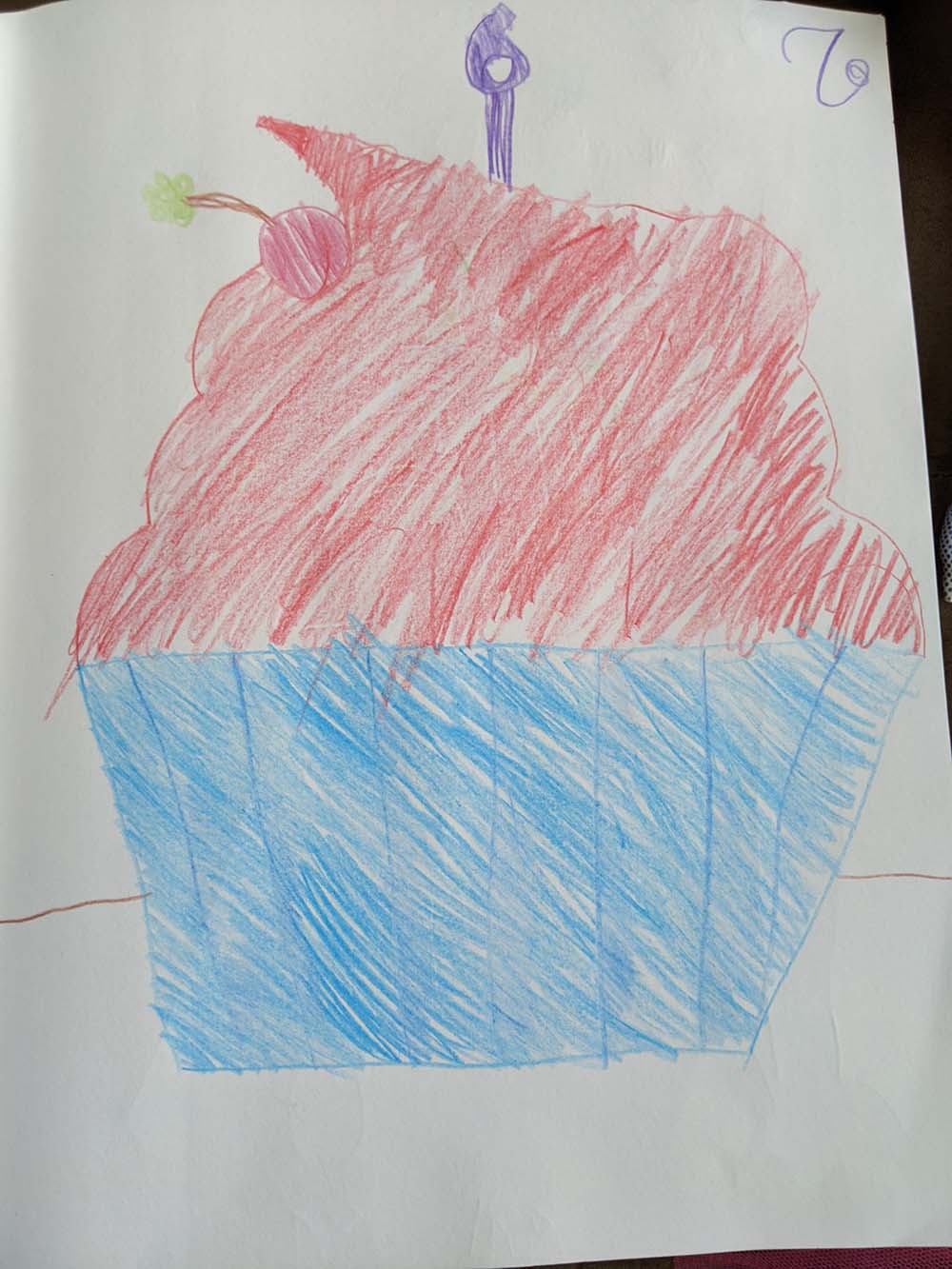 A cupcake with a blue wrapper, red frosting, a pink cherry, and a candle with a number 6 on it.